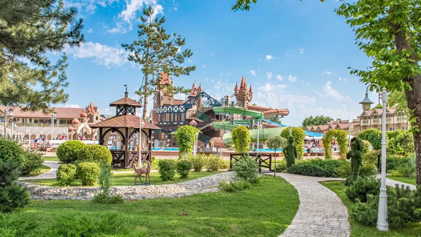 Территория семейного отеля Alean Family Doville с аквапарком, бассейнами, деревянной беседкой и ландшафтным дизайном на фоне сказочных замков.