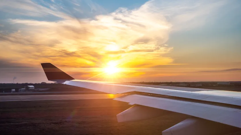 Вид из иллюминатора самолета на крыло и взлетно-посадочную полосу аэродрома во время заката