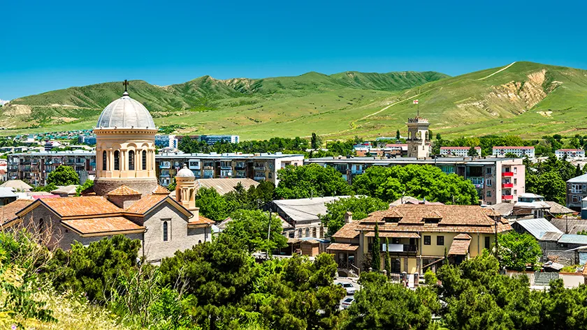 Панорамный вид на архитектуру грузинского города Гори на фоне зеленых холмов в ясный день.